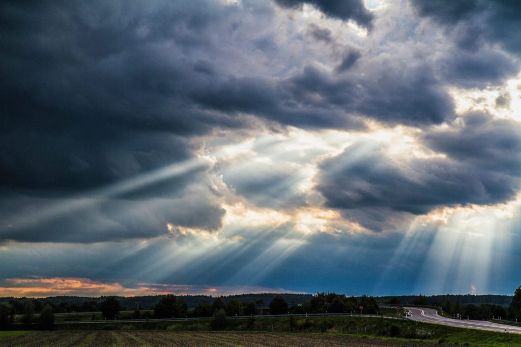 Sunlight streaming through dark storm clouds over a rural road and field